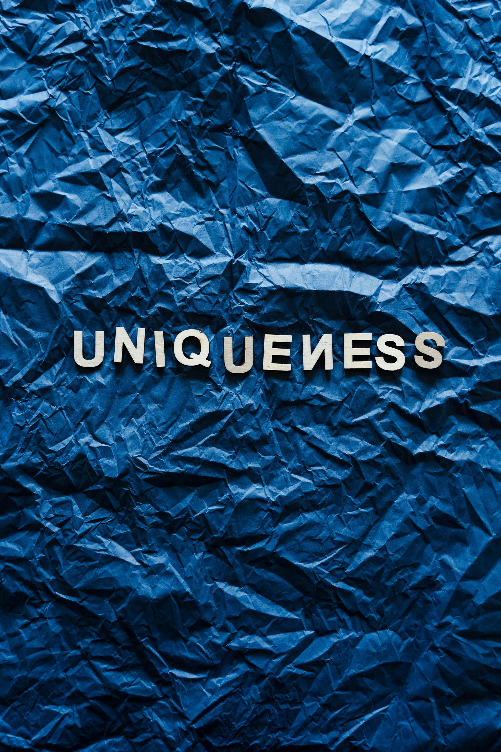 Uniqueness text on blue crumpled paper representing brand differentiation